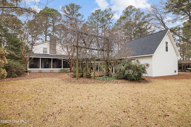 rear view of house with roof with shingles, a sunroom, and a chimney