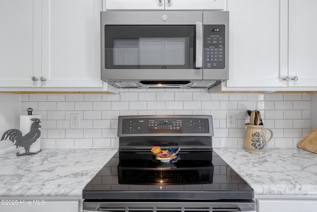 kitchen with electric stove, light stone counters, stainless steel microwave, backsplash, and white cabinetry