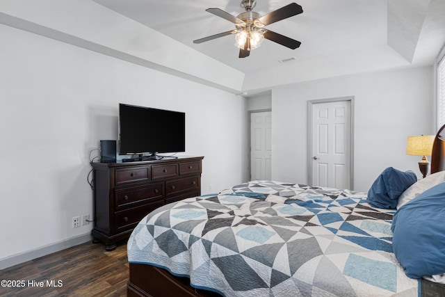 bedroom with visible vents, ceiling fan, baseboards, a tray ceiling, and dark wood-style flooring