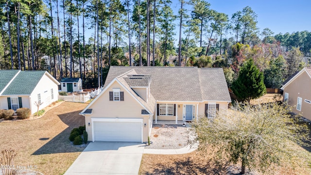 view of front facade featuring a garage, roof with shingles, concrete driveway, and fence