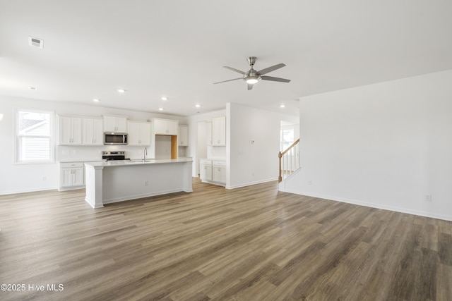 unfurnished living room with light wood finished floors, baseboards, stairway, recessed lighting, and a sink