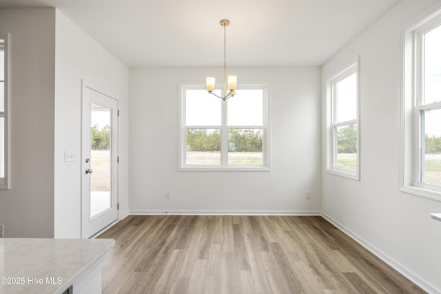 unfurnished dining area with baseboards, a notable chandelier, and light wood-style flooring