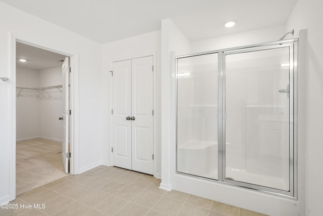 bathroom featuring tile patterned floors, a stall shower, a spacious closet, and baseboards