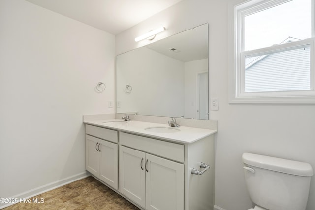 bathroom with double vanity, toilet, baseboards, and a sink