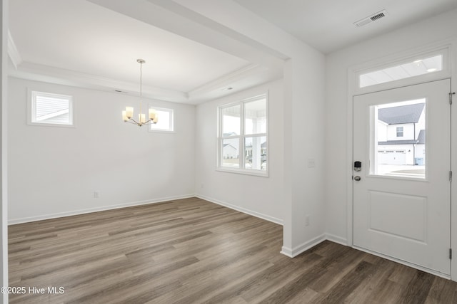 foyer entrance with visible vents, wood finished floors, baseboards, an inviting chandelier, and a raised ceiling