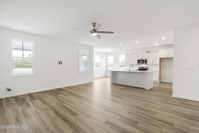 unfurnished living room with a sink, wood finished floors, recessed lighting, baseboards, and ceiling fan