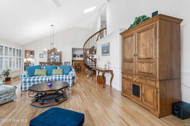 living room with ceiling fan with notable chandelier, high vaulted ceiling, stairs, and light wood finished floors