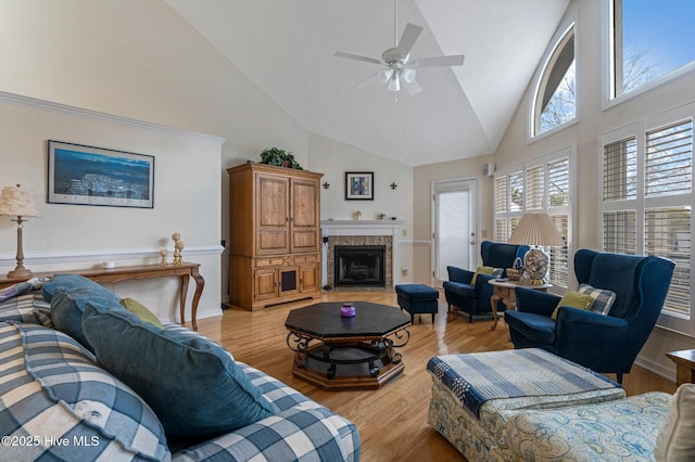 living room featuring a ceiling fan, a fireplace, light wood finished floors, and high vaulted ceiling