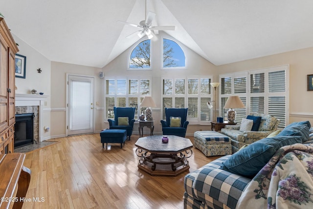 living room with high vaulted ceiling, a ceiling fan, light wood finished floors, and a tile fireplace