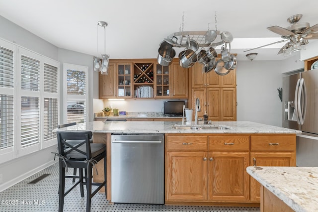 kitchen featuring light stone countertops, a sink, stainless steel appliances, glass insert cabinets, and pendant lighting