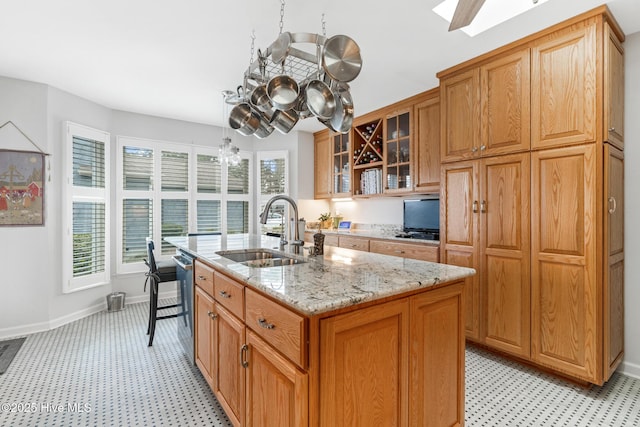 kitchen with light stone countertops, a skylight, an island with sink, a sink, and glass insert cabinets