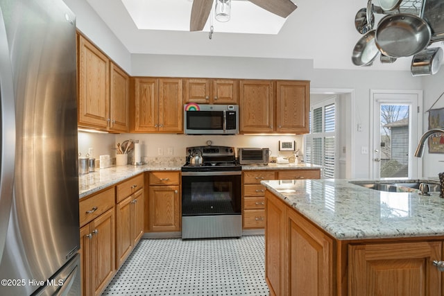 kitchen featuring a ceiling fan, a sink, appliances with stainless steel finishes, a skylight, and light floors