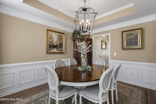 dining area with dark wood finished floors, a raised ceiling, a notable chandelier, and wainscoting