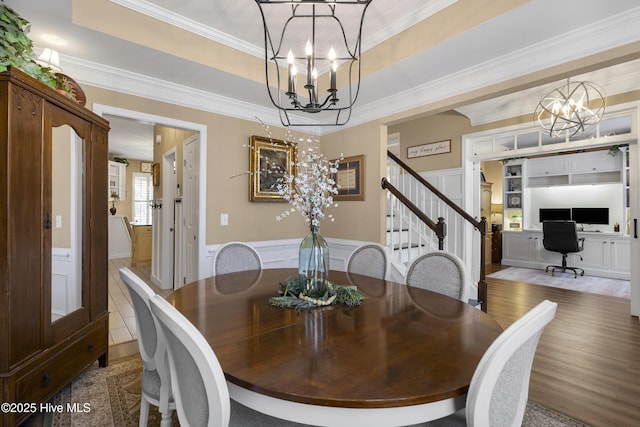 dining area featuring a tray ceiling, a chandelier, ornamental molding, and a decorative wall