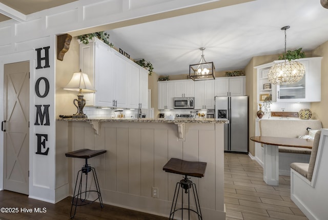 kitchen with a peninsula, stainless steel appliances, white cabinets, a notable chandelier, and tasteful backsplash