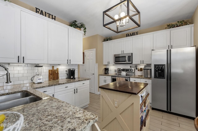 kitchen with backsplash, a chandelier, appliances with stainless steel finishes, white cabinets, and a sink