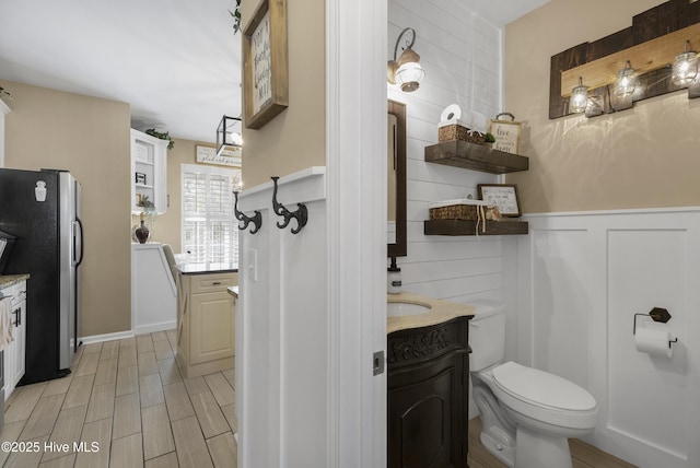 bathroom with wainscoting, toilet, vanity, and wood finish floors