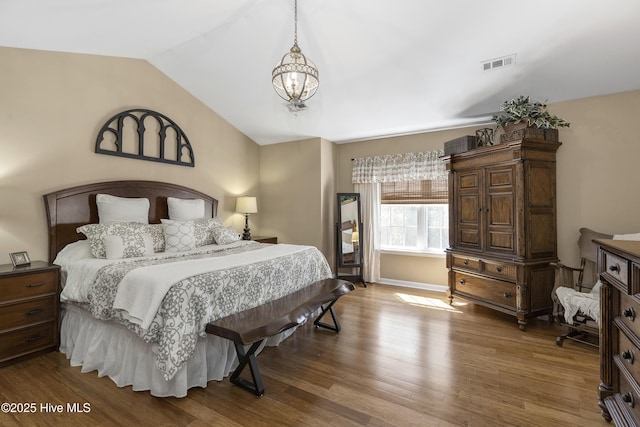 bedroom with vaulted ceiling, a notable chandelier, wood finished floors, and visible vents