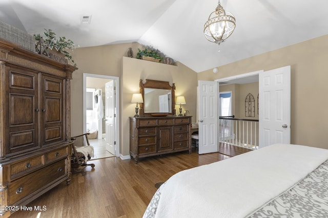 bedroom with dark wood-style floors, visible vents, ensuite bath, vaulted ceiling, and a chandelier