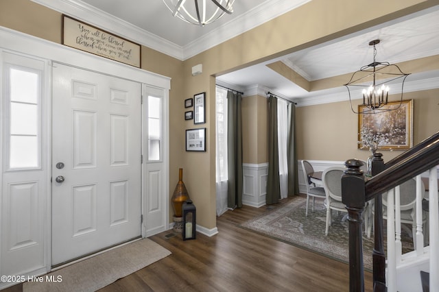 entryway featuring dark wood finished floors, crown molding, a notable chandelier, and a wainscoted wall