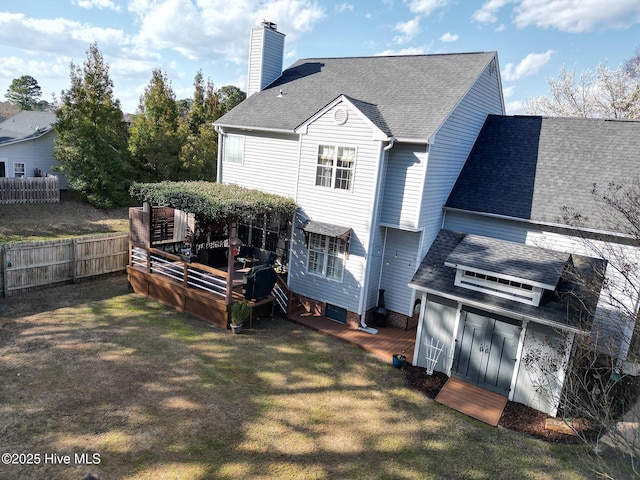 rear view of property featuring fence, roof with shingles, a lawn, a chimney, and a deck