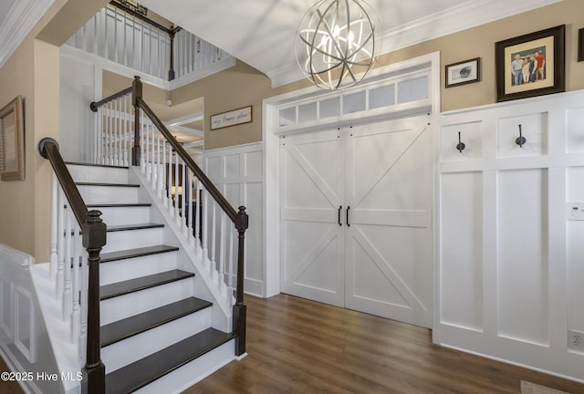 foyer entrance featuring stairs, ornamental molding, an inviting chandelier, dark wood-style floors, and a decorative wall