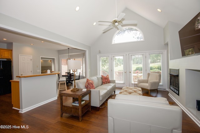 living area with a fireplace, high vaulted ceiling, dark wood-type flooring, and ceiling fan