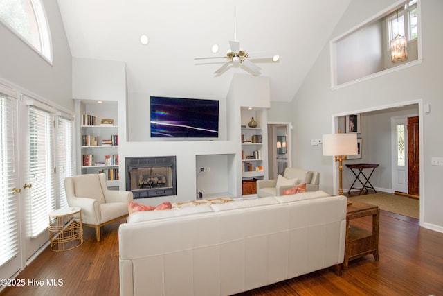 living area featuring built in shelves, a ceiling fan, wood finished floors, high vaulted ceiling, and a fireplace