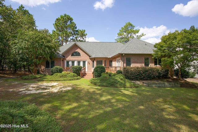 single story home featuring a deck, a front lawn, brick siding, and roof with shingles