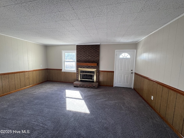 unfurnished living room featuring a fireplace, wood walls, carpet floors, and ornamental molding