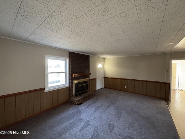 unfurnished living room featuring a fireplace, a wainscoted wall, and carpet floors