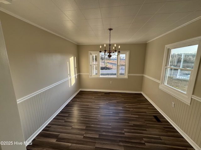 unfurnished dining area with a wainscoted wall, an inviting chandelier, dark wood-style flooring, and crown molding