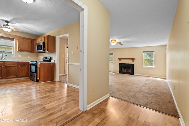 kitchen featuring ceiling fan, a sink, light countertops, stainless steel appliances, and brown cabinets