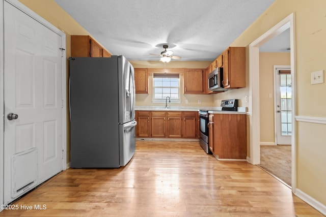 kitchen featuring light wood-type flooring, light countertops, appliances with stainless steel finishes, a textured ceiling, and brown cabinets