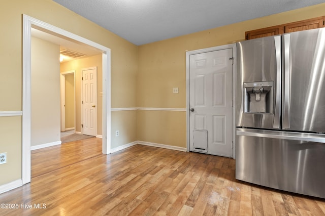 kitchen featuring visible vents, baseboards, light wood-style flooring, brown cabinetry, and stainless steel fridge