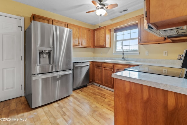 kitchen with brown cabinetry, a sink, stainless steel appliances, light countertops, and light wood-style floors