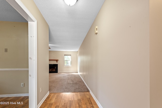 corridor featuring a textured ceiling, light wood-type flooring, and baseboards