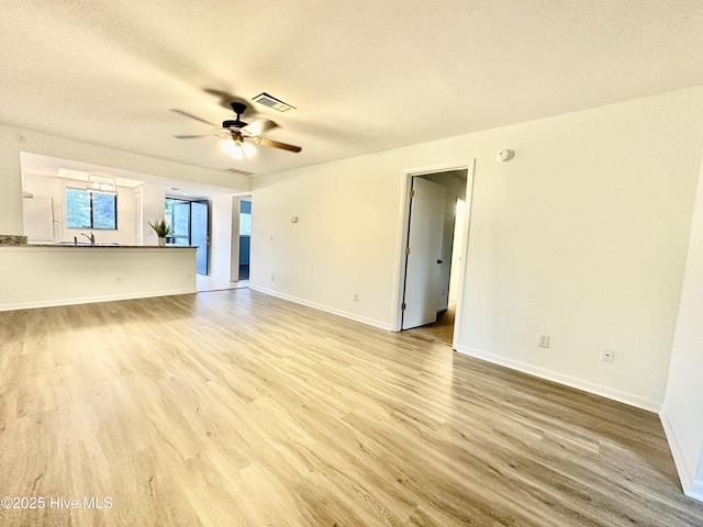 unfurnished living room with visible vents, baseboards, ceiling fan, wood finished floors, and a sink