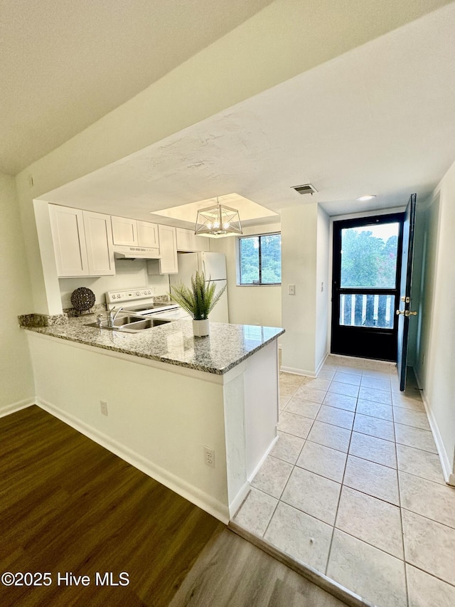 kitchen with visible vents, light stone counters, a peninsula, white cabinets, and white appliances