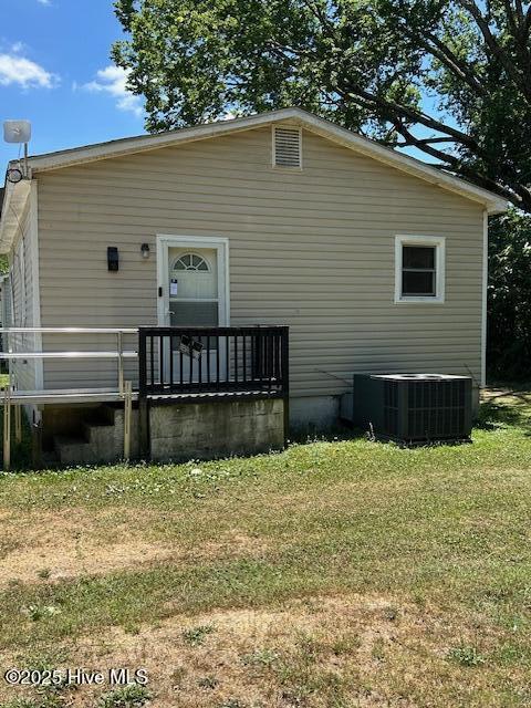 rear view of property with central AC unit and a lawn