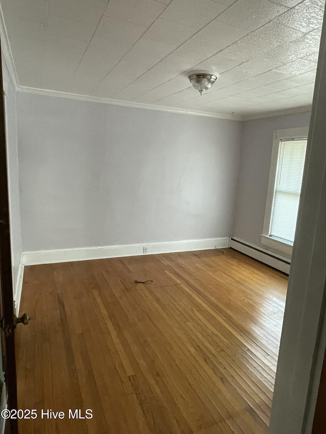 spare room featuring a baseboard heating unit, wood finished floors, baseboards, and ornamental molding