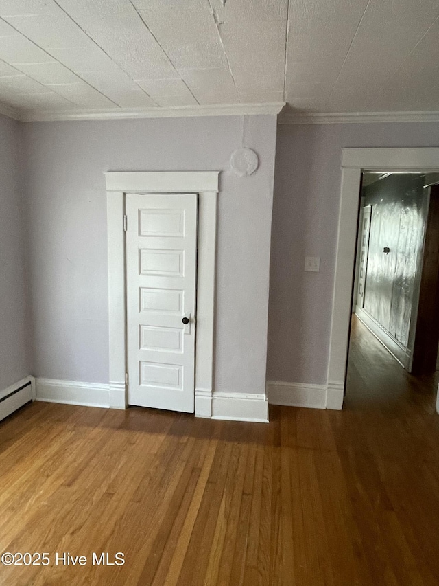 empty room featuring baseboard heating, wood finished floors, baseboards, and ornamental molding