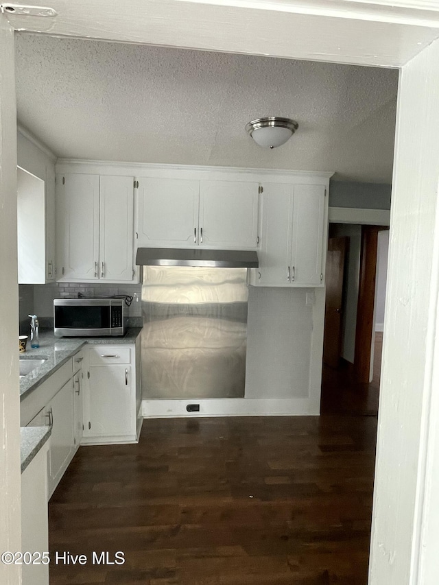 kitchen with stainless steel microwave, white cabinetry, under cabinet range hood, dark wood finished floors, and a textured ceiling