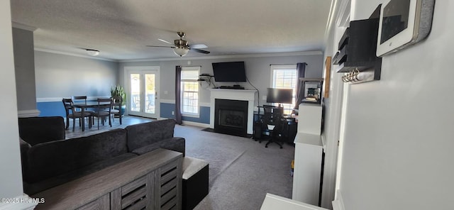 carpeted living room featuring a fireplace with flush hearth, a textured ceiling, a ceiling fan, and ornamental molding