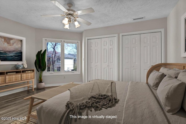 bedroom featuring wood finished floors, visible vents, ceiling fan, a textured ceiling, and two closets