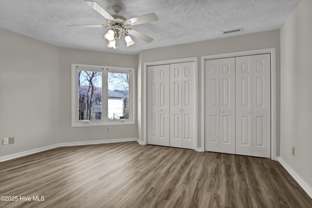 unfurnished bedroom featuring visible vents, two closets, a textured ceiling, wood finished floors, and baseboards