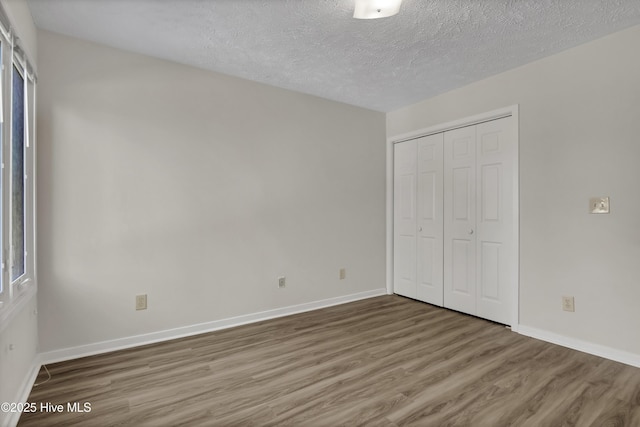 unfurnished bedroom with a closet, baseboards, a textured ceiling, and wood finished floors