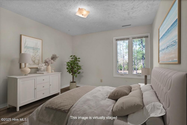 bedroom featuring visible vents, a textured ceiling, dark wood-type flooring, and baseboards