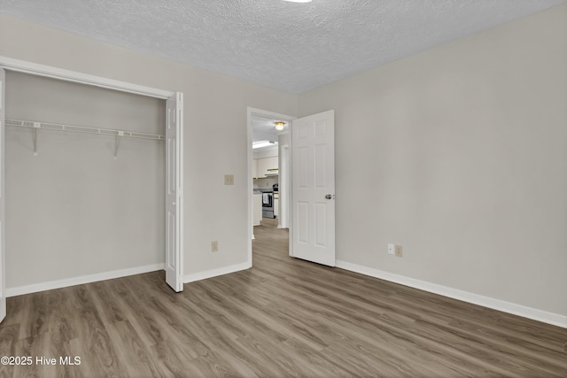 unfurnished bedroom with a closet, baseboards, a textured ceiling, and wood finished floors