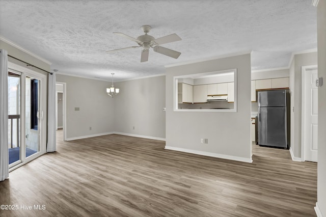 unfurnished living room featuring ceiling fan with notable chandelier, crown molding, wood finished floors, and baseboards